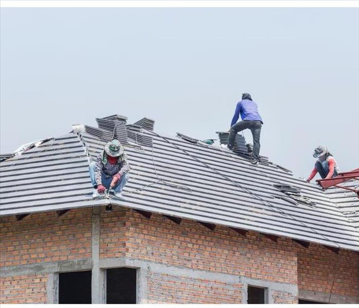Workers installing concrete tiles on the roof while roofing house in construction site