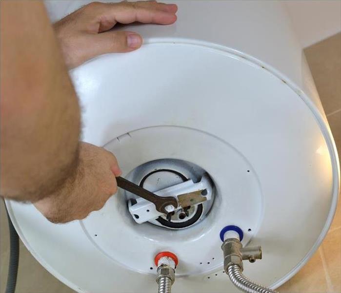 Man's hands unscrewing a screw-nut on a water heater with a wrench on a boiler