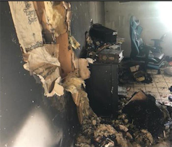 torn drywall damaged by fire, chair and a black cabinet